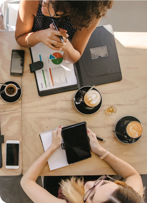Break Coffee Franchise 7 Overhead shot of two women sitting at a table and working. Between them are several cups of fresh coffee.