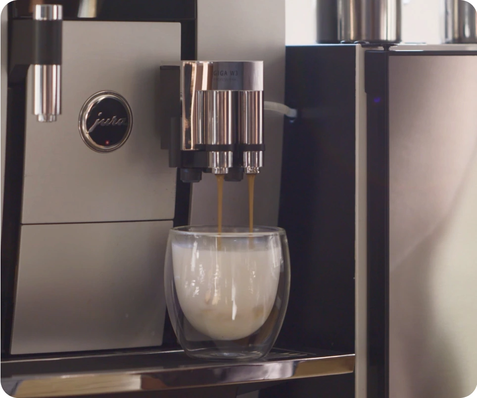Break Coffee Franchise 8 A glass coffee mug full of freshly steamed milk sitting under a coffee machine.